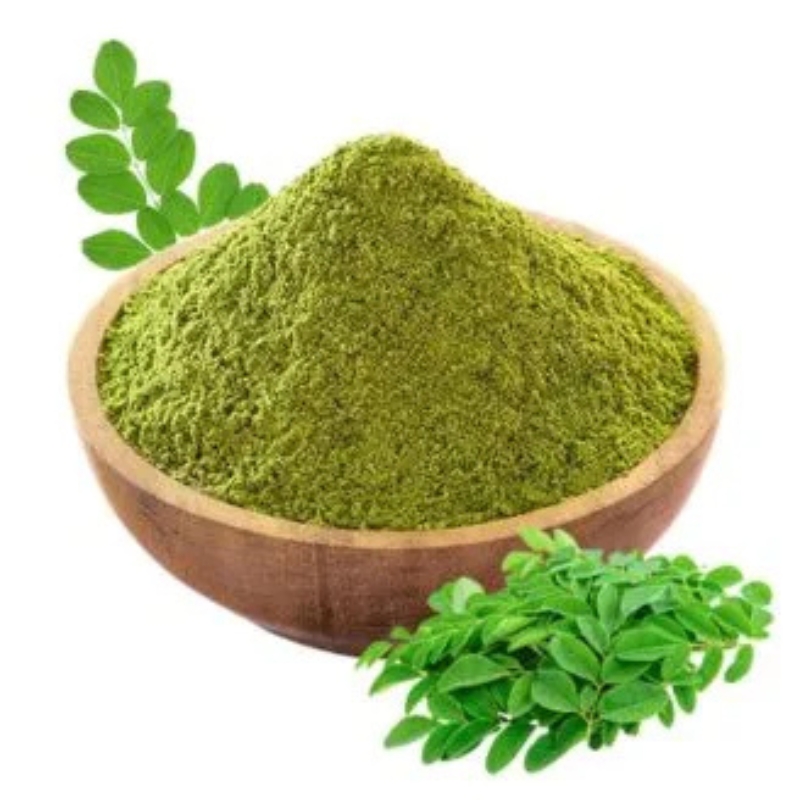 Moringa leaf powder in a wooden bowl with fresh moringa leaves placed beside it.