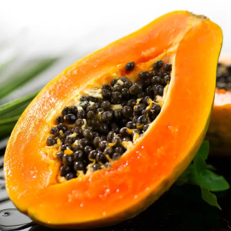 Ripe papaya cut in half showing orange flesh and black seeds.