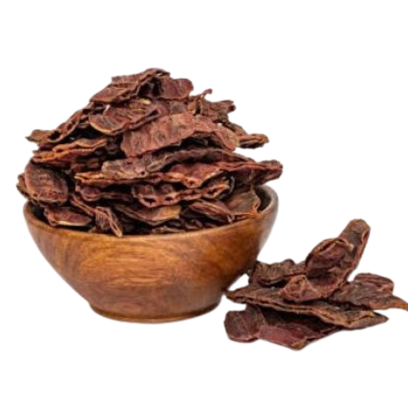 Dried shikakai pods stacked in a wooden bowl with additional pods placed beside it..
