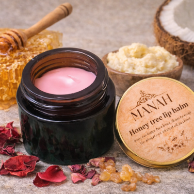 Open jar of Manah Honey Tree Lip Balm surrounded by raw honeycomb, dried rose petals, coconut, and Mahua butter, highlighting its all-natural, honey-based, deeply moisturising, chemical-free formulation.